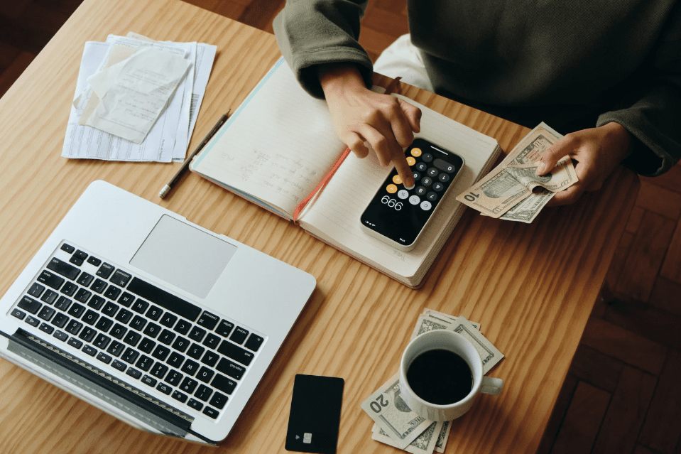 Person managing finances with calculator, laptop, and cash
