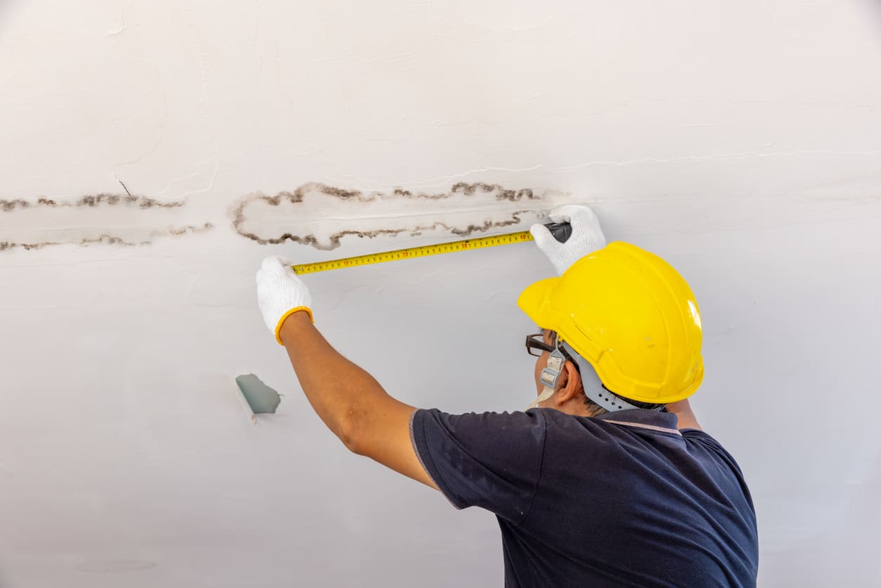 Worker measuring ceiling water damage with tape measure.