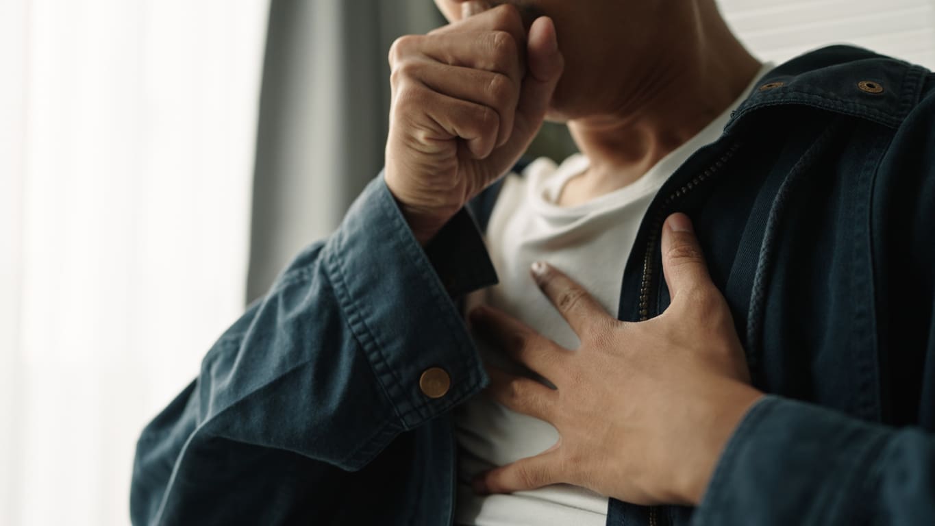 Person coughing and holding chest in discomfort.