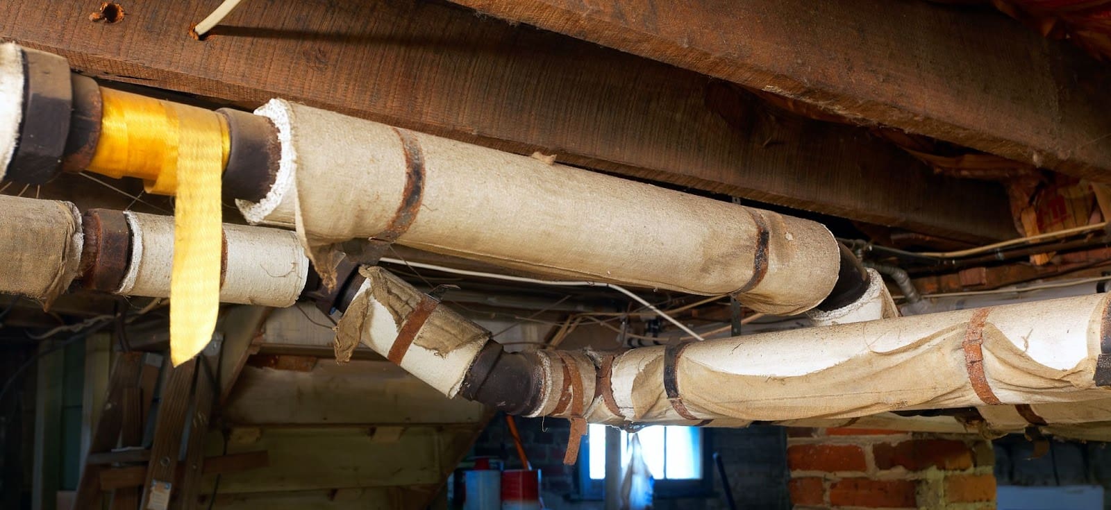 Old insulation on basement pipes with wooden beams