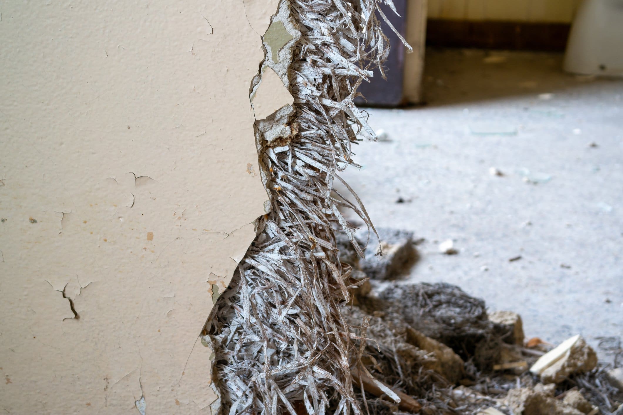 Close-up of damaged drywall with exposed asbestos fibers.