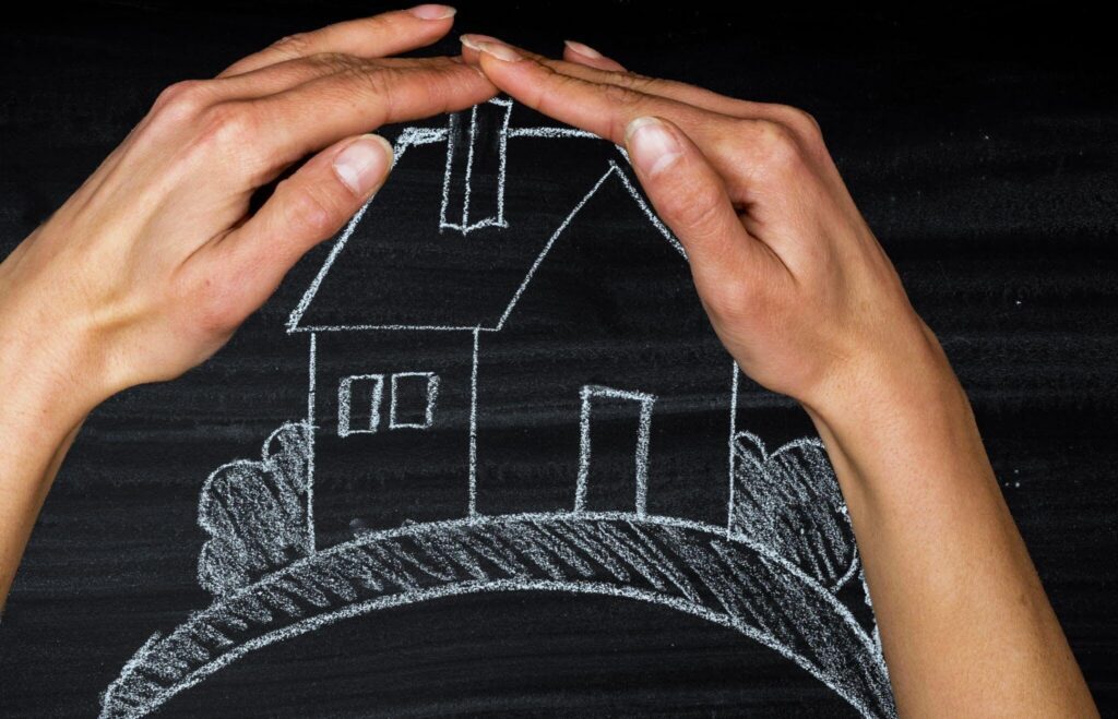 Hands protecting chalk house drawing on blackboard