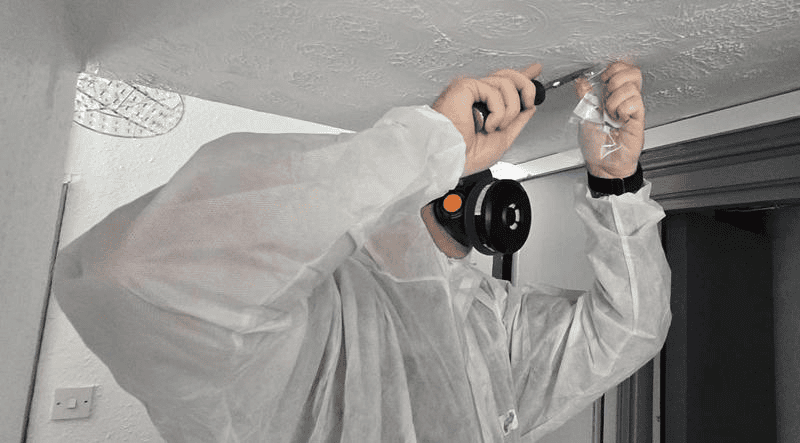 Worker in protective suit scraping ceiling